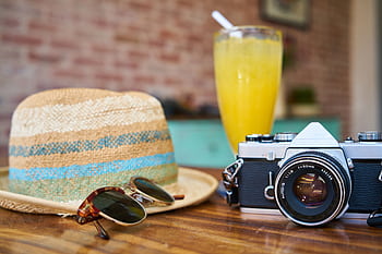 A stylish scene showcasing a vintage camera, hat, and orange juice, evoking summer travel vibes. HD wallpaper