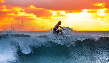 Surfer riding a wave during a stunning sunset, capturing the thrill of water sports. HD wallpaper