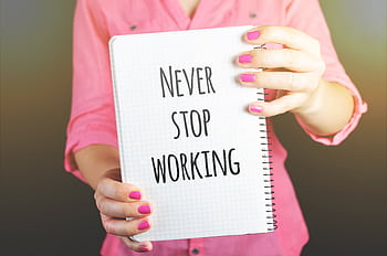 A woman holding a notebook with the motivational message 'Never Stop Working' indoors. HD wallpaper