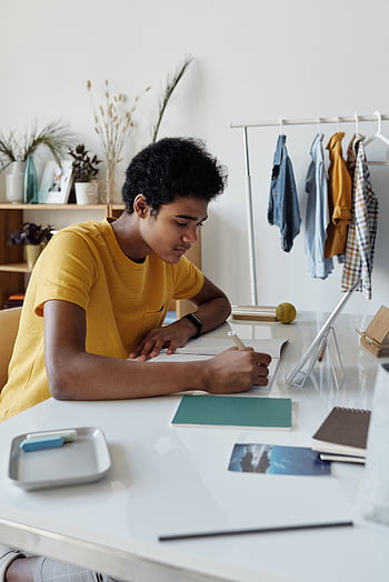 Focused African American teen studying indoors with a tablet and notebook at home. HD phone wallpaper