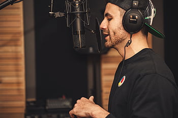 A man wearing heads and recording vocals in a music studio with a micro. HD wallpaper