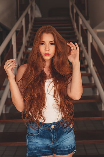A stylish woman with long red hair poses on stairs in casual attire. HD phone wallpaper