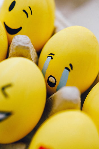 Close-up of yellow Easter eggs painted with emoji faces in an egg carton, showcasing creativity and fun. HD phone wallpaper