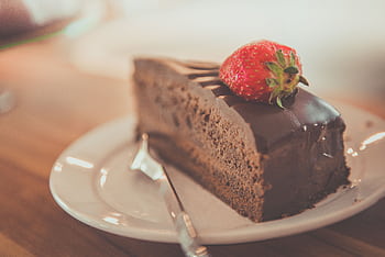 Close-up of a delectable chocolate cake slice topped with a fresh strawberry on a plate. HD wallpaper