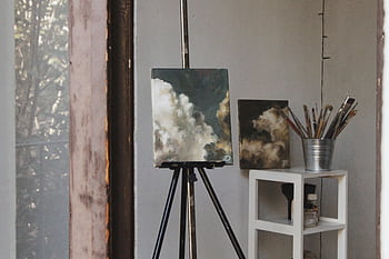 Cozy art studio featuring cloud paintings on easels and paintbrushes, captured indoors. HD wallpaper