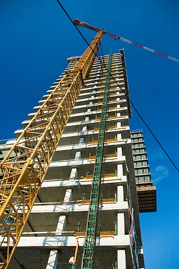 Low-angle view of skyscraper under construction with crane, clear blue sky. HD phone wallpaper