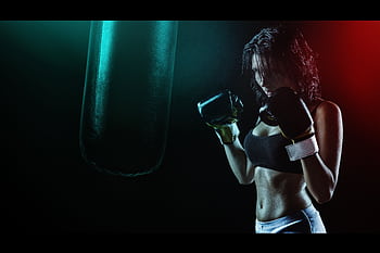 Powerful of a woman boxer preparing to train with a punching bag in a dramatic dark setting. HD wallpaper