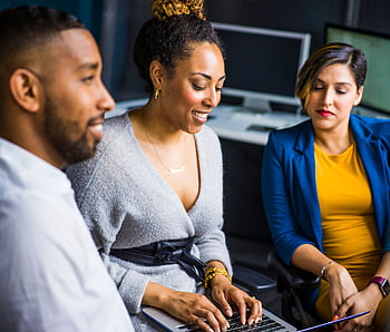 A diverse group of colleagues collaborates on a project using a laptop in a modern office setting. HD wallpaper