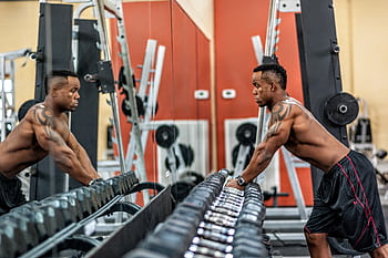 Muscular man exercising with dumbbells in gym, emphasizing strength and fitness. HD wallpaper