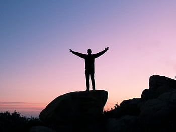 Silhouette of a man on a rock with arms raised, embracing the sunset sky. HD wallpaper