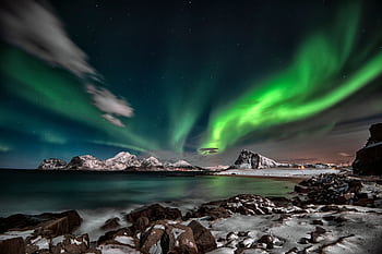 Mesmerizing aurora borealis illuminating a winter landscape with snowy mountains and a starry sky. HD wallpaper