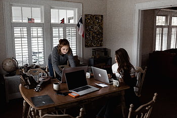 Two young women working collaboratively in a cozy home office setting. HD wallpaper