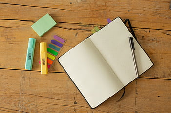 Top view of open notebook, pen, highlighters, and sticky notes on a wooden desk. HD wallpaper