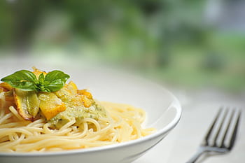 Close-up of freshly made spaghetti topped with basil and creamy pesto sauce in a white dish. HD wallpaper