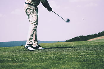 A golfer in mid-swing on a sunny day at the golf course, showing motion and focus. HD wallpaper