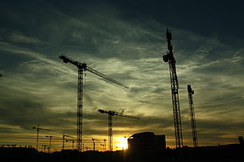 Silhouetted cranes at a construction site during sunset, showcasing industrial growth. HD wallpaper