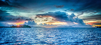 Vibrant sunset over tropical ocean with dramatic clouds and distant island. HD wallpaper