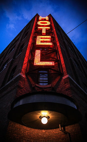 Eye-catching low angle shot of a neon hotel sign illuminating a brick building facade at dusk. HD phone wallpaper