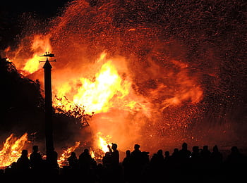 A large fire illuminates the night as people watch, surrounded by smoke and sparks. HD wallpaper