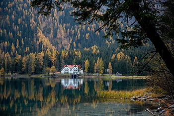 Discover a peaceful autumn scene with a cottage by a tranquil lake, surrounded by colorful trees. HD wallpaper