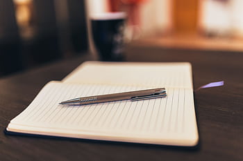 Open notebook with pen on a table, mug in background, cozy setting. HD wallpaper