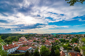A scenic aerial view of a que village with red-roofed houses under a dramatic sky. HD wallpaper