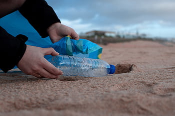 Hands collecting a plastic water bottle from the sandy beach, promoting environmental awareness. HD wallpaper