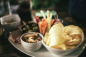 A tempting snack platter featuring crisps, vegetables, and olives, perfect for a casual gathering. HD wallpaper