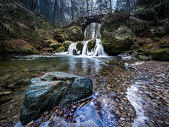 Beautiful waterfall cascading under a rustic stone bridge in a serene forest setting. HD wallpaper