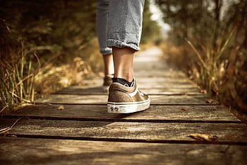 Person wearing sneakers walking on a wooden path in a sunlit park. HD wallpaper