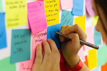 Hands writing on colorful sticky notes during a brainstorming session indoors. HD wallpaper