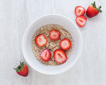 A fresh and nutritious breakfast bowl featuring oats topped with sliced strawberries. HD wallpaper