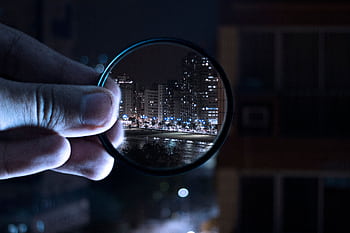 A hand holding a lens filter enhances a vibrant city nightlife scene. HD wallpaper