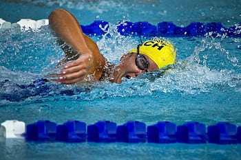 Swimmer wearing a yellow cap and goggles competing in a swimming pool HD wallpaper