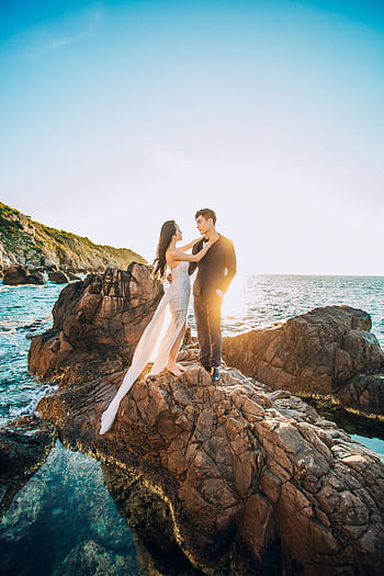 A couple posing on rocky seaside for a wedding hoot in Vietnam under a clear sunny sky. HD phone wallpaper