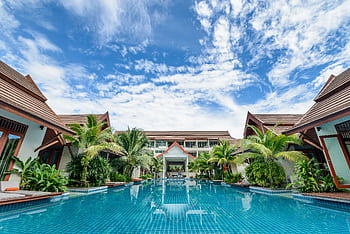 Spacious swimming pool surrounded by tropical villas under a bright blue sky, perfect for relaxation. HD wallpaper