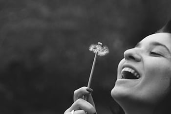 A joyful woman smiling while blowing on a dandelion in a black and white portrait. HD wallpaper