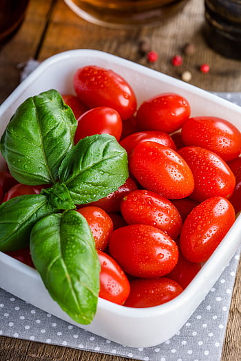 A bowl of vibrant cherry tomatoes garnished with fresh basil leaves on wooden background. HD phone wallpaper