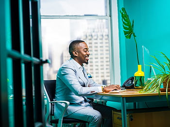 Confident businessman in modern office working on laptop with city view. HD wallpaper