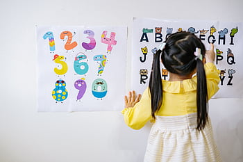 Young girl in kindergarten learning numbers and alphabets with colorful posters. HD wallpaper