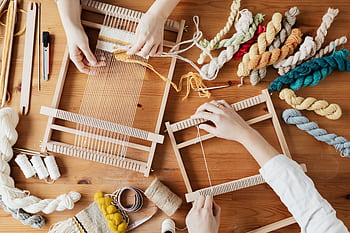 Hands weave yarn on looms in a vibrant workshop, showcasing creative craftsmanship with colorful threads. HD wallpaper