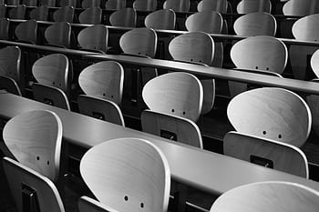 A monochrome view of empty wooden seats in a spacious lecture hall displaying symmetry and design. HD wallpaper