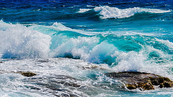 Vibrant blue ocean waves crashing against rocky shoreline under clear summer skies. HD wallpaper
