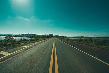 A tranquil highway stretches into the horizon under a clear blue sky, offering a serene travel vibe. HD wallpaper