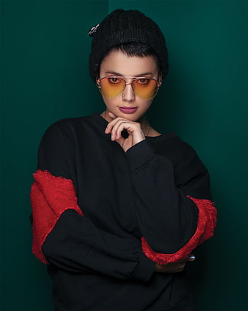Elegant portrait of a woman in sunglasses and a knit cap with a green background. HD phone wallpaper