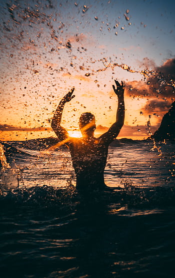 Silhouette of a person enjoying the ocean at sunset, creating a dynamic seascape scene. HD phone wallpaper
