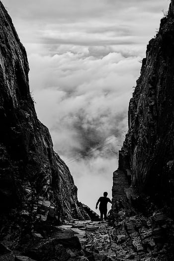 Silhouette of a climber navigating rugged cliffs against a cloud-filled sky. HD phone wallpaper