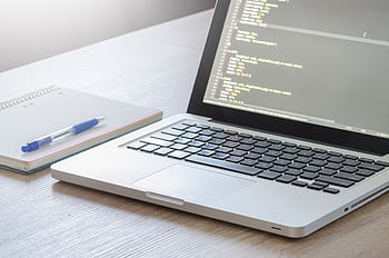 Laptop with code editor open, notebook and pen on wooden desk, perfect for tech and work themes. HD wallpaper