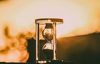 Close-up of an hourglass capturing the essence of time against a sunset backdrop. HD wallpaper