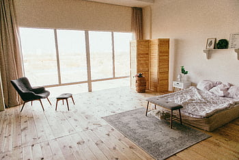 Elegant minimalist bedroom with wooden floors, large windows, and chic furniture, exuding a warm, inviting ambiance. HD wallpaper
